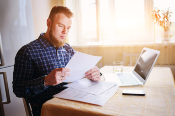Fototapeta premium Businessman at home, he is working with a laptop, checking paperwork and bills