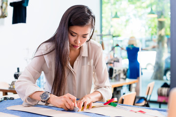 Fototapeta premium Asian fashion designer woman drafts cut pattern in her workshop