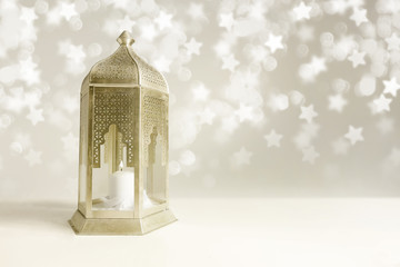 Ornamental golden Arabic lantern on the table with glittering star-shaped bokeh lights. Greeting card for Muslim community holy month Ramadan Kareem. Festive blurred background with empty space. © tabitazn