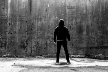 Man In A Black Hoodie and Jeans Facing A Concrete Wall