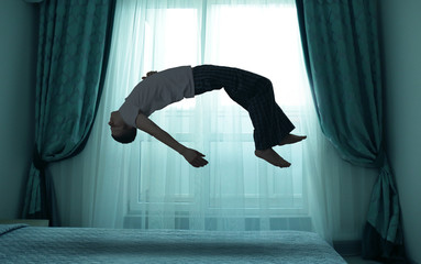 Sleep paralysis concept. Young man levitating over bed - obrazy, fototapety, plakaty