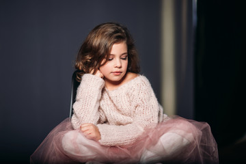 Little beautiful girl with brown hair in a light sweater and with a skirt of tulle.Studio. A princess poses for a photographer.