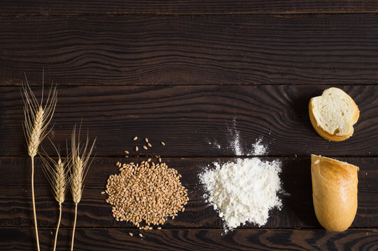Wheat ears, grains, flour and sliced bread on a dark wooden table