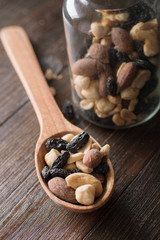 Spoon with jar full of nuts and raisins on a wooden background. Top view.