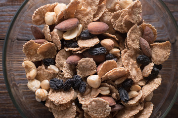 Oat flakes in bowl with mix of nuts and dry fruits on wooden background. Close up.