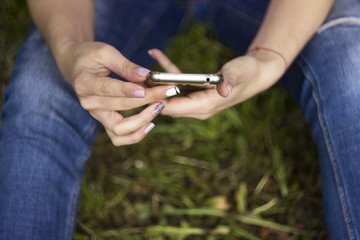 The girl in jeans and a t-shirt sitting on the grass and gaining a message on the phone