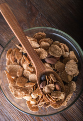 Oat flakes in bowl and wooden spoon with mix nuts and dry fruits on wooden background. Top view