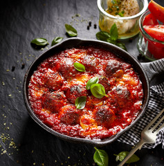 Meatballs in tomato sauce with addition cheese and fresh basil on iron pan, black background