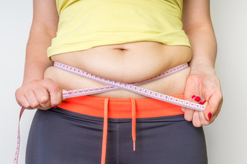 Overweight woman with tape is measuring fat on belly