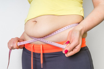 Overweight woman with tape is measuring fat on belly