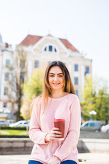 Portrait of young beautiful woman sitting in city street bench outdoor drinking coffee