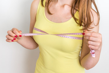 Slim woman measures her breast with a measuring tape