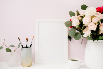Home office desk with photo frame mockup, beautiful roses and eucalyptus bouquet in front of pale pastel pink background. Blog, website or social media concept .