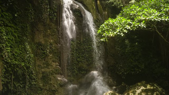Beautiful waterfall in green forest in jungle. Waterfall with natural swimming pool in a mountain river canyon. Philippines, Bohol. 4K video.