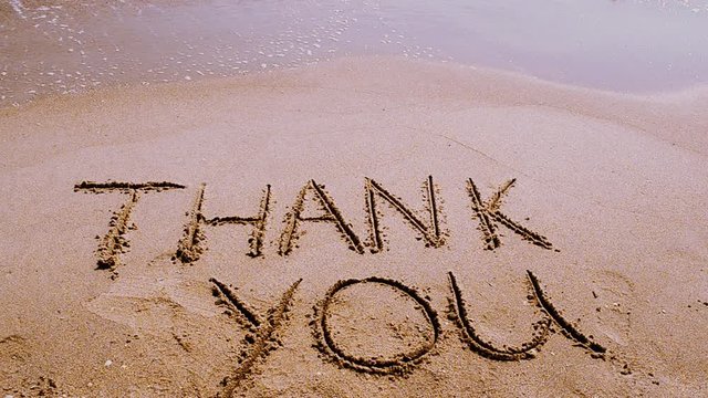 Thank you handwritten in sand on a beach.