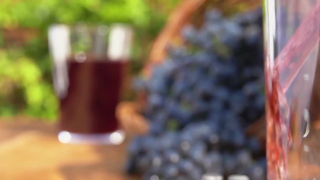 Grape juice is pouring into a glass on a background of a basket of ripe grapes