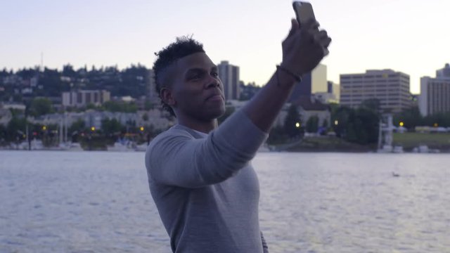Man Stands On A Dock And Takes Selfies, Beautiful View Of City In Background