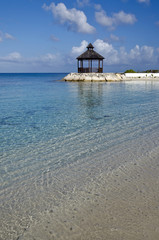 Clear warm water, blue sky, and a beach-side gazebo in the Caribbean