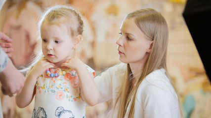 Mom helps her daughter to wear colored beads in shop for kids