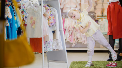 Little girl in a summer suit has fun in front of the mirror in the children's clothing store
