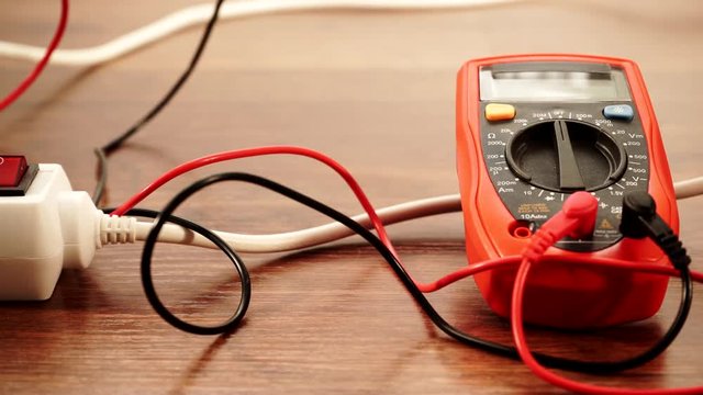 Measurement of voltage in electrical socket extension cord with multimeter on wooden floor background 4K ProRes HQ codec