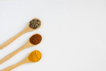 Turmeric, Paprika and Black Pepper in wooden spoon over white background.