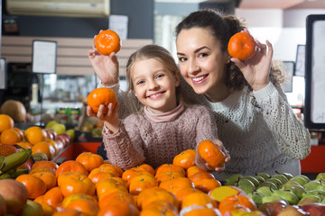 blonde girl with mother buying mandarins in shop