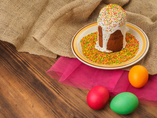 Easter cake, ceramic bowl with colorful sweet powder and easter colored egg. Russian and Ukrainian, orthodox slavic traditional Easter kulich on rural background. Old wood, red mesh paper and burlap.