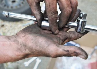 mains pleine de cambouis d'un mécanicien tenant un outil