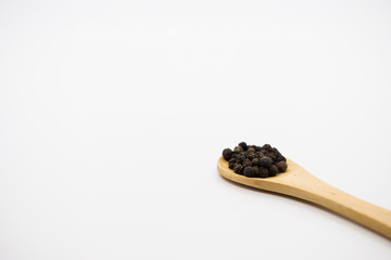 Black Peppercorn in wooden spoon over white background.