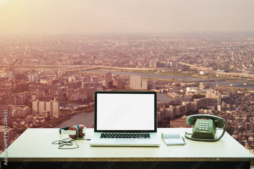 Poster laptop computer with blank empty screen on table in office and cityscape blur background.