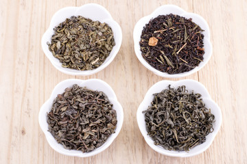 Green and black tea leaves in ceramic bowl on wood background