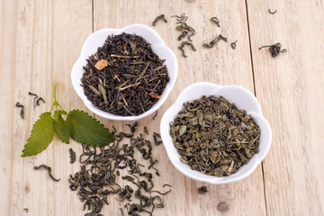 Green and black tea leaves in ceramic bowl on wood background