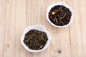 Green and black tea leaves in ceramic bowl on wood background