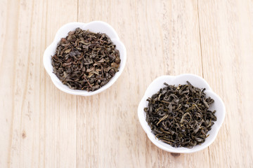 Green and black tea leaves in ceramic bowl on wood background