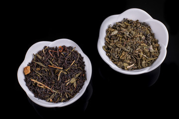 Green and black tea leaves in ceramic bowl on black background