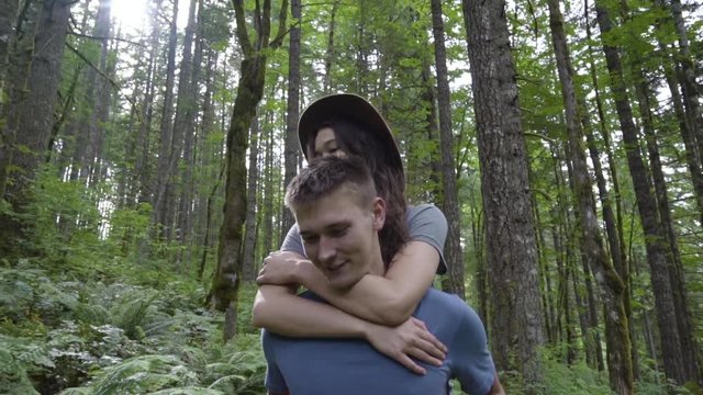 Man Gives Girlfriend A Piggyback Ride Through The Forest, Closeup Of Them Smiling 
