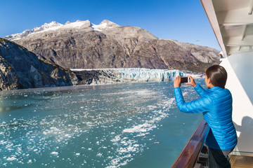 Alaska cruise tourist taking photo of Glacier Bay. Ship passenger on balcony looking at view taking...