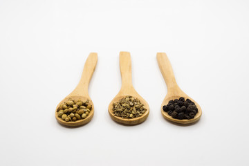 Black pepper, cumin and coriander in wooden spoon over white background.