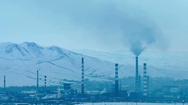 Wide shot of operating factory with smoking chimneys against snow-capped mountains background.Time lapse clouds floating by.