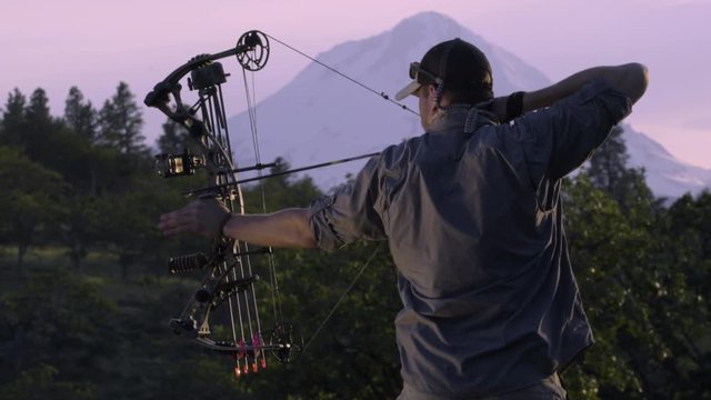 Elk Hunter Practices Using His Compound Bow At Sunset In The Mountains