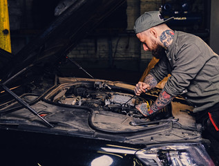 Bearded tattooed mechanics near car in a garage.