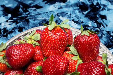 fresh ripe useful fruit strawberry in a clay bowl closeup on a marble dark blue background
