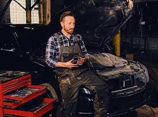 Fototapeta na wymiar Bearded tattooed mechanics near car in a garage.