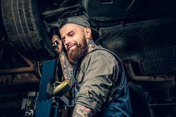 Fototapeta Bearded  mechanic working with the car's chassis in a workshop. obraz