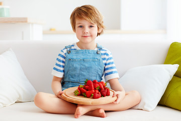 cute kid sitting on couch with a tray of tasty, ripe strawberry