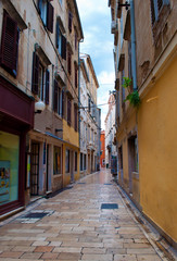 Cozy and empty narrow street between two stone houses with doors and shutters on a summer morning. Zadar center, Croatia