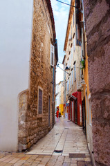 Cozy and empty narrow street between two stone houses with shutters on a summer morning. Zadar center, Croatia