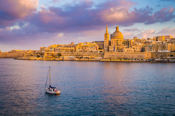 Fototapeta premium Valletta, Malta - St.Paul's Cathedral in golden hour at Malta's capital city Valletta with sailboat and beautiful colorful sky and clouds