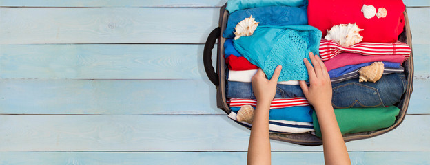 Woman packing luggage for a new journey on a wooden floor. Place for your text.